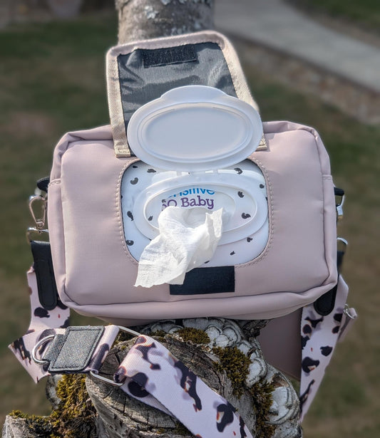 Pink diaper bag with a lid open, showing wipes inside, attached to a tree branch outdoors